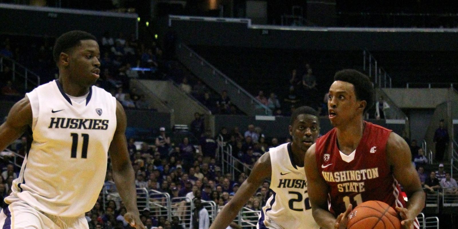 A college guard dribbling the ball low as two defenders close in