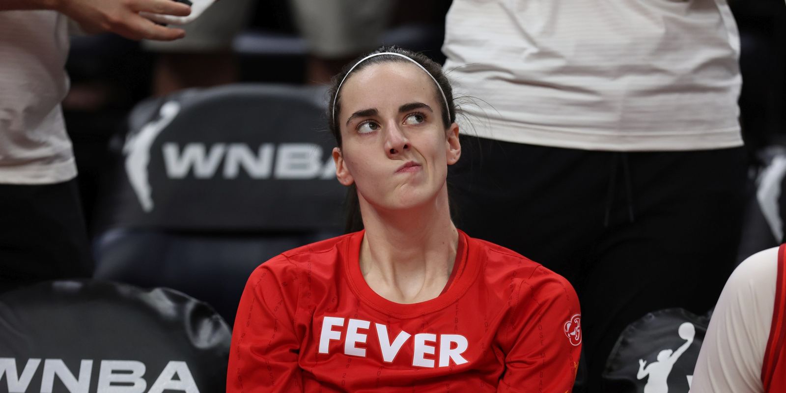 Caitlin Clark in a red Indiana Fever shirt sitting on the bench