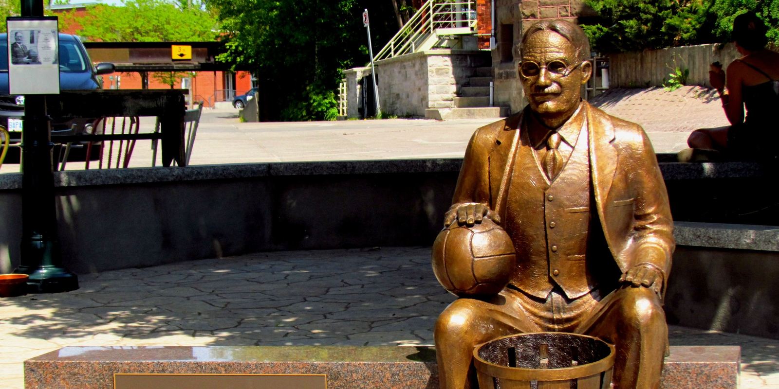 A bronze statue of James Naismith seated with a ball and a peach basket