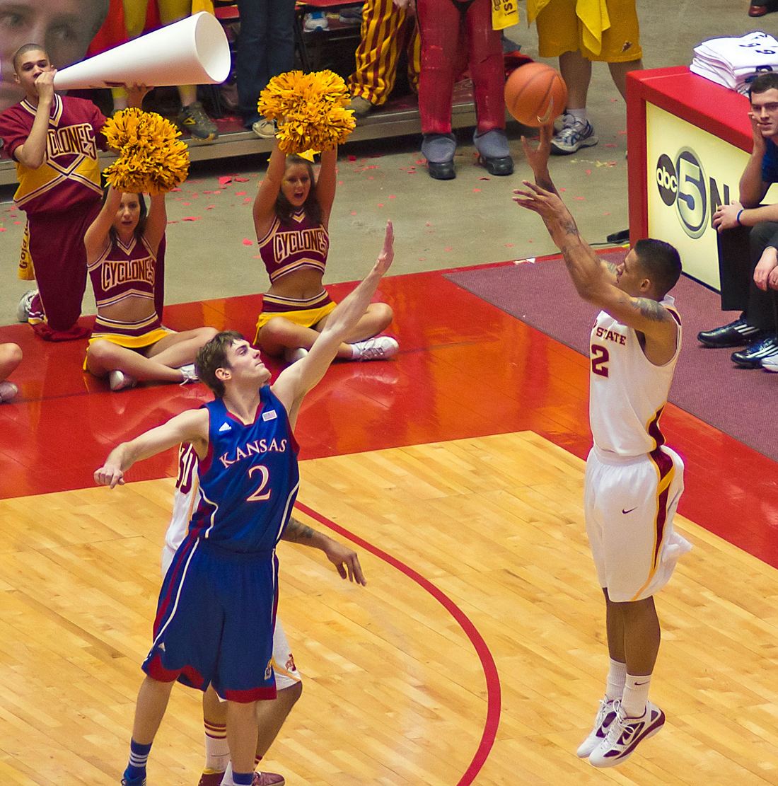 A college player releasing a three-pointer as a defender contests