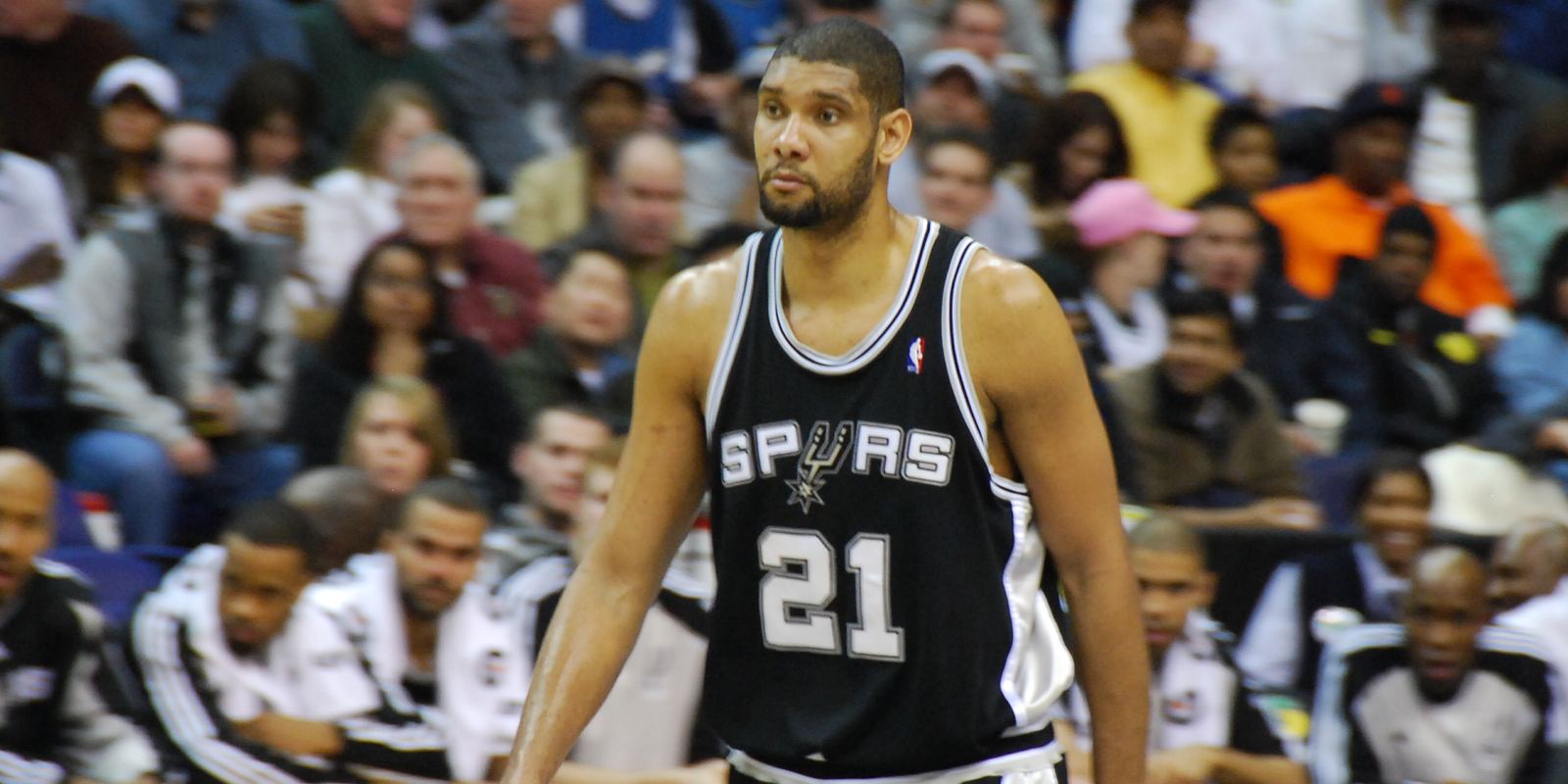 Tim Duncan in a black Spurs number 21 jersey walking on court
